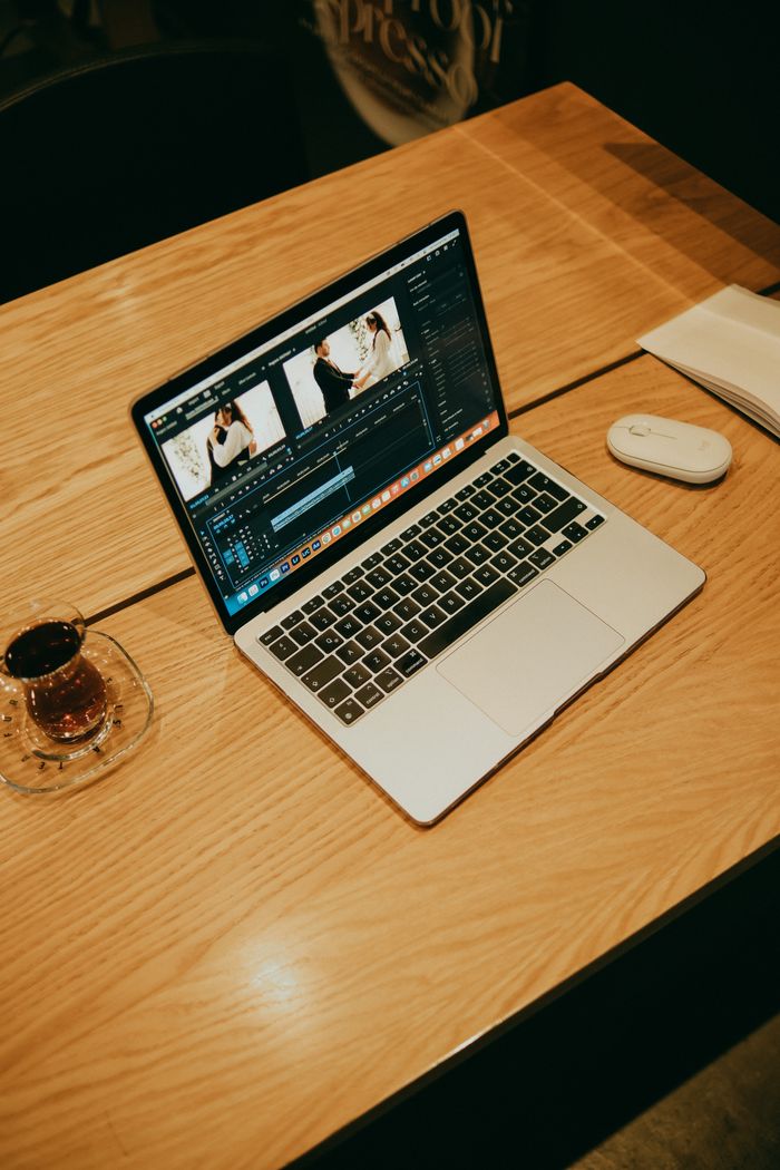 Un ordinateur portable sur une table en bois dans un café, affichant un logiciel de montage vidéo pour un travail créatif.