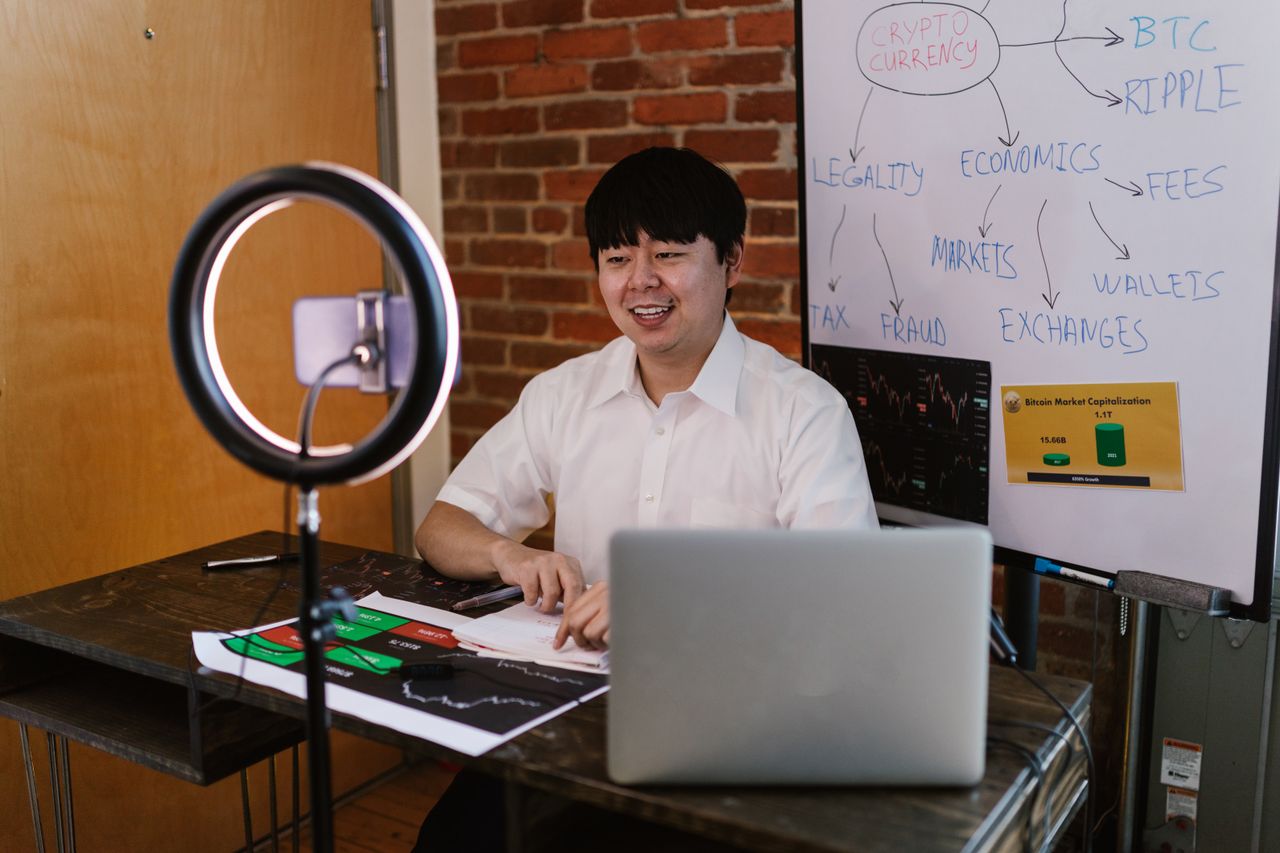 Un homme discutant d’économie des cryptomonnaies avec une ring light et un ordinateur portable, dans une démarche de création de contenu engageant.